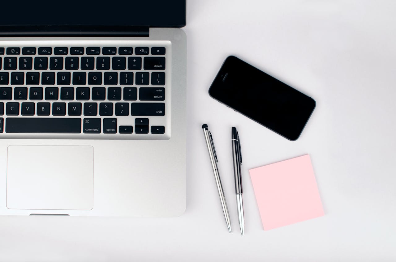 Home Overhead view of a sleek workspace featuring a laptop, smartphone, and stationeries on a white desk.